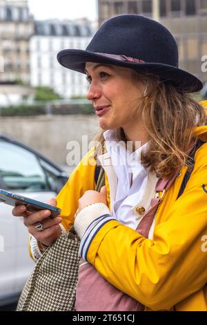 Young smiling woman in hat holding smartphone - Paris, France. Stock Photo