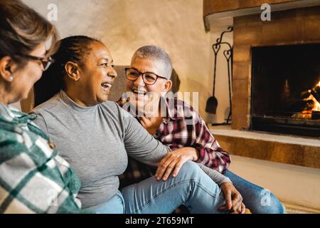 Multiracial senior friends by wood fireplace having fun together at rural home. Winter and fall season life style concept Stock Photo