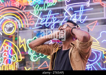 Delighted carefree male with sunglasses dances in rhythm of melody, closes eyes listens loud song in headphones. People, music, emotions concept. Stock Photo