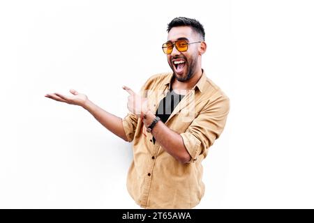 Excited happy positive young latin man, student pointing aside with fingers hand gesture at copy space advertising product, presenting sale discount p Stock Photo