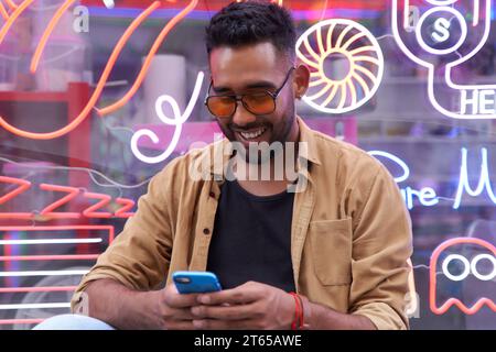 Happy latin man in casual clothes using smartphone, hispanic guy chatting online, using new mobile app, texting with friend Stock Photo