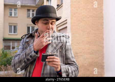 A man smokes a cigarette and drinks alcohol on a city street. Alcohol and nicotine. Unhealthy Lifestyle Stock Photo