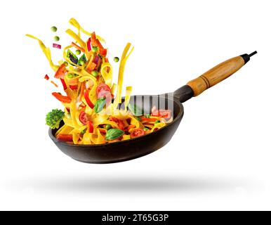 Cooking Italian pasta with vegetables flying over a hot frying pan isolated in white. The concept of food levitation Stock Photo