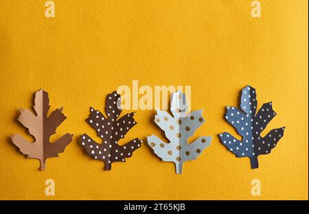 Four colourfil  leaves cut out of paper lie on a solid yellow background with space for text above. The leaves are bwown, grey and dotted.  The concep Stock Photo