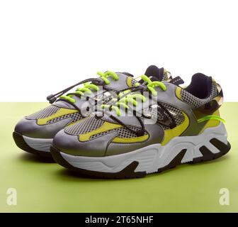 Female fashionable metallic grey running shoes with bright green laces and yellow and silver details on the white and green background. Advertising co Stock Photo