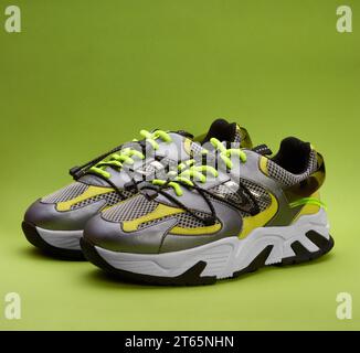 Close up view of women's fashionable metallic grey running shoes with bright green laces and yellow and silver details on the gradient green backgroun Stock Photo
