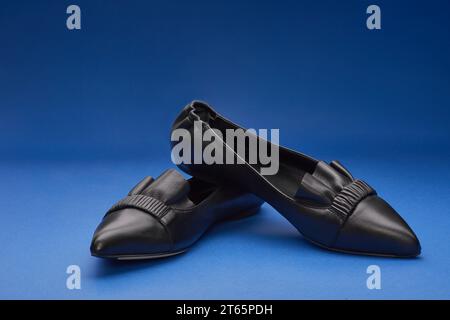 Elegant black pointed-toe leather ballet flats with wrinkled and ruffle details on the blue gradient background. Copy space. Creative minimalistic lay Stock Photo