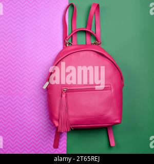 Contemporary women's pinkish-red leather backpack with a handle and zipped compartment with tassel pull isolated on a fun contrasting pink-green backg Stock Photo