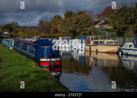 Narrowboats (barges, flat bottomed boats) and small sailing boats moored up at the side of the Leeds Liverpool canal in Bingley, West Yorkshire. Stock Photo