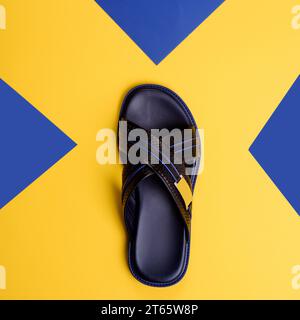 Trendy criss-cross black-blue male slipper with embossing design isolated on a graphic yellow-blue background with copy space. Mock-up for online fash Stock Photo