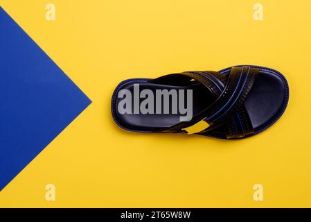 Stylish criss-cross black-blue men's slipper with embossing design isolated on a yellow-blue background with copy space. Fashion blogger content. Crea Stock Photo