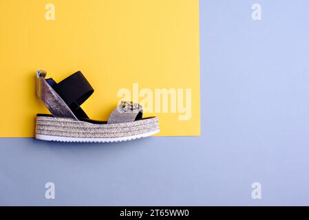 Side view of stylish silver and black platform sandals with big rhinestones on the front on a yellow-blue paper background with copy space. Summer sea Stock Photo