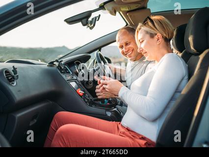 Happy smiling two young adulds couple using smartphone navigation inside car during auto jorney.They are laughing during road trip. Family, couples re Stock Photo