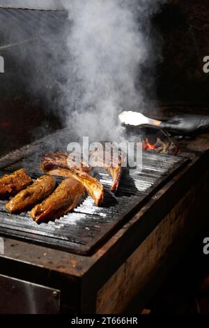 Appetizing juicy tomahawk steaks, ribeye and sirloin laid out on a barbecue grill over a burning flame while grilling. Grilled meat in a restaurant. Stock Photo