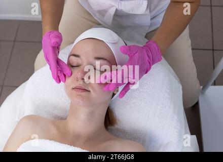 Young Woman Receives Spa Facial Massage Treatment In Spa Salon. Relax And Stress Relief. Professional Skin Care Therapist Takes Care Of Female Patient Stock Photo