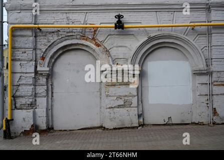 A yellow gas pipe with a black faucet against a gray brick wall Stock Photo