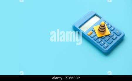 Concept of under construction or fixing for financial, loan, or budget. Safety cone or traffic cone over a calculator on blue background with copy spa Stock Photo