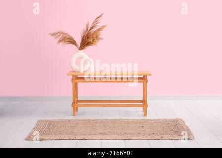 Wooden table with pampas grass in vase near pink wall Stock Photo