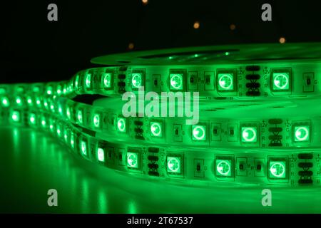 Bobbin with roll of glowing LED strip lighting placed on table, green color in dark room Stock Photo