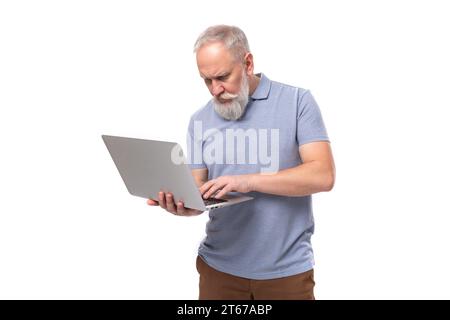 stylish pensioner man with beard and mustache in shirt and trousers holding laptop and working remotely Stock Photo