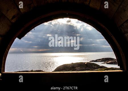 View from window of abandoned lighthouse on sea against sun. Spider made web on window and caught a lot of midges. Sun's rays fall like fan from cloud Stock Photo