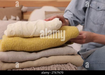 Woman with stack of different folded blankets and clothes on bed, closeup. Home textile Stock Photo