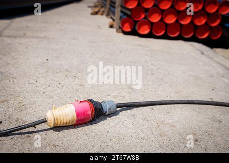 Extension cord for distribution power, plugs and socket providing electrical energy to construction site. Package of new plastic water pipes stacked o Stock Photo