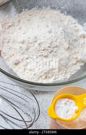 A teaspoon of baking powder ready to be added to a bowl of flour Stock Photo