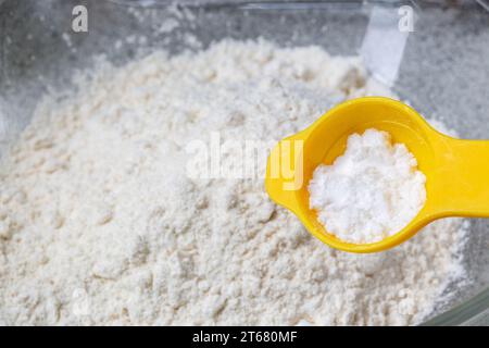 A yellow teaspoon with Cream of tartar above a bowl of white flour. Stock Photo