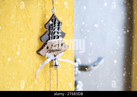 A Christmas tree-shaped pendant with the inscription merry Christmas hangs on the front door of the house on a bell with retro wiring with snow. Copy Stock Photo