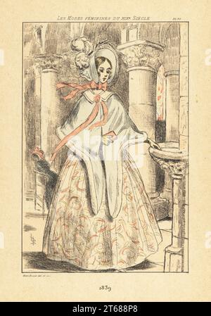 Fashionable woman blessing herself with holy water from a font inside an old Gothic church, Paris, 1839. She wears a bonnet tied with a ribbon, fur-lined capelet, dress with full skirts. Handcoloured drypoint or pointe-seche etching by Henri Boutet from Les Modes Feminines du XIXeme Siecle (Female Fashions of the 19th Century), Ernest Flammarion, Paris, 1902. Boutet (1851-1919) was a French artist, engraver, lithographer and designer. Stock Photo