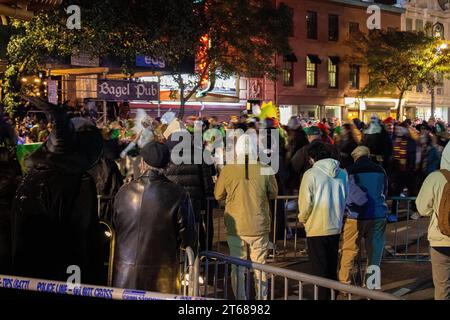 A nighttime view of a bustling cityscape, showcasing a large crowd of people gathered around barriers on a city street Stock Photo