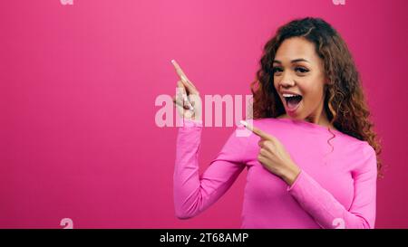 Smiling young women points two fingers to copy space, Valentine's Day promotion Stock Photo