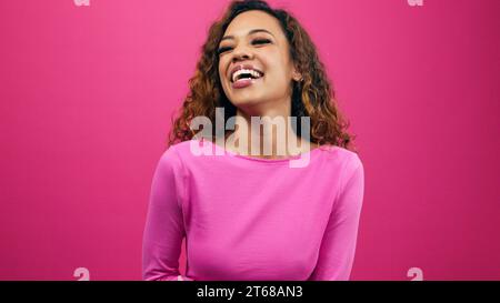 Happy young woman laughing in pink studio, wearing pink for Valentine's Day Stock Photo