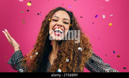 Beautiful young woman dances while multi-coloured confetti rains down Stock Photo