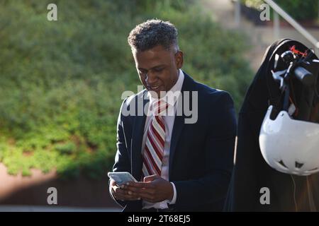 A young businessman in a suit standing on the sidewalk and looking at his mobile phone Stock Photo