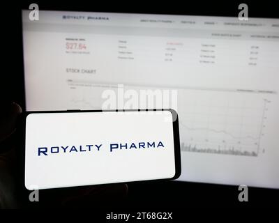 Person holding mobile phone with logo of American biopharmaceutical royalties company Royalty Pharma in front of web page. Focus on phone display. Stock Photo