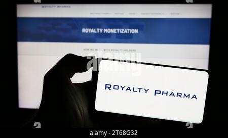 Person holding smartphone with logo of US biopharmaceutical royalties company Royalty Pharma in front of website. Focus on phone display. Stock Photo