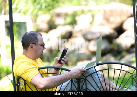 A young adult male wearing a yellow shirt is sitting in a comfortable spot, typing away on a laptop Stock Photo