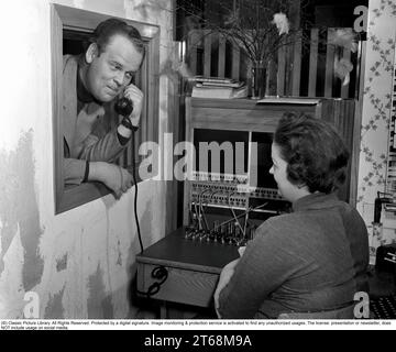 Arne Mattsson. 1919-1995, Swedish director, known for having directed films such as She danced one summer, Hemsöborna and Körkarlen. Here with a telephone receiver to the ear and a female operator who works in the company's switchboard. She connects the incoming and outgoing calls to the right person using cords for the respective telephones in a telephone switchboard. Sweden 1952 Kristoffersson ref 34K-40 Stock Photo