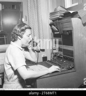 A female operator who works in the company's switchboard. She connects the incoming and outgoing calls to the right person using cords for the respective telephones in a telephone switchboard. Sweden 1954 Kristoffersson ref BO71-9 Stock Photo