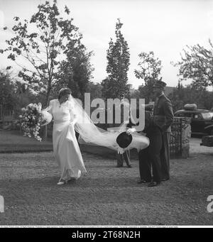 A wedding in 1941. The bride is helped with the long bridal veil by the groom outside the church. It must be fixed and look beautiful for the upcoming wedding. Sweden 1941. Kristoffersson ref 199-11 Stock Photo