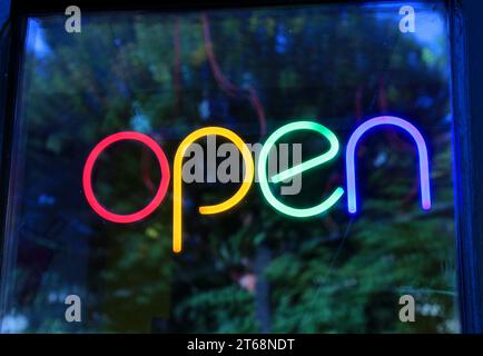 Neon sign saying "open" with letters of different colors. Front window. Stock Photo