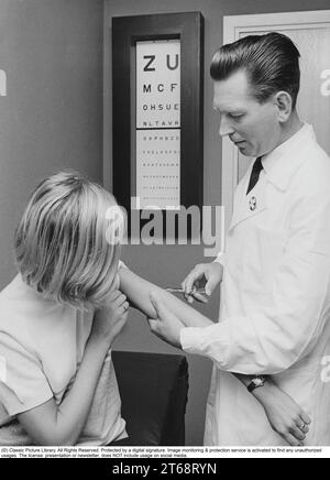 Vaccines in the 1960s. A doctor gives a young boy a vaccine shot in 1964. Vaccines are given against diseases such as: Tetanus, Whooping Cough, Polio, Measles, Rubella etc. Stock Photo