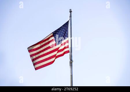 American flag waving in wind on flag pole. The national red, white and blue star stiped USA flag flying. The US flag is a symbol of freedom and pride Stock Photo