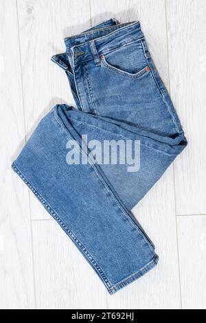 Blue jeans folded on white wooden background, denim folded on light wooden background - top view Stock Photo