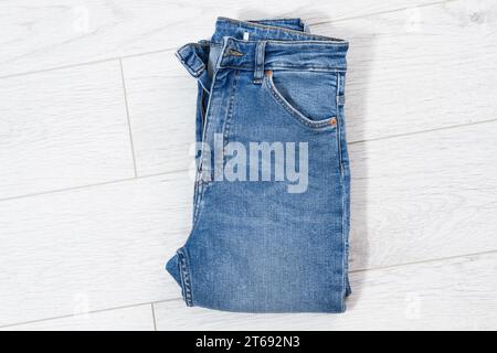 Blue jeans folded on white wooden background, denim folded on light wooden background - top view Stock Photo