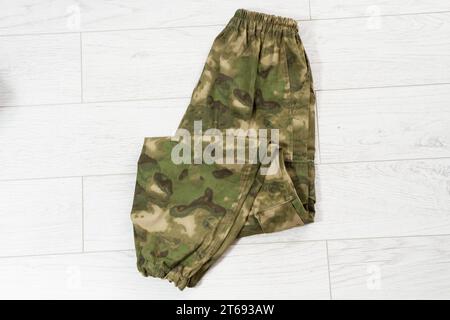 Closeup Camouflage pants on wooden background, green khaki pants. Unfolded camouflage soldier elastic pants on wooden background. Stock Photo