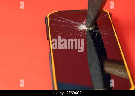 hammer breaking the screen of a mobile phone on a red background Stock Photo