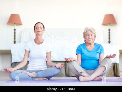 Rejuvenating the spirit. Senior woman sits in the lotus position while doing yoga with her trainer. Stock Photo